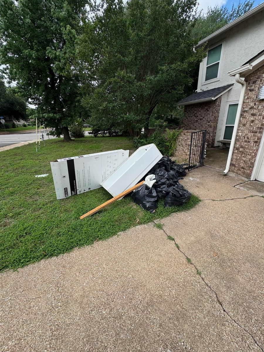 Bathtub, a long cardboard box, lumber and black trash bags piled on a front lawn