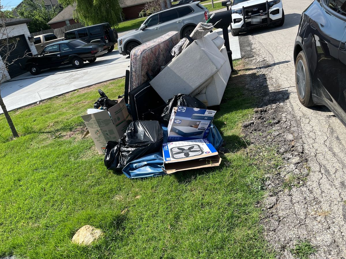 Mattress, couch, trash bags and boxes piled on a front lawn at the curb