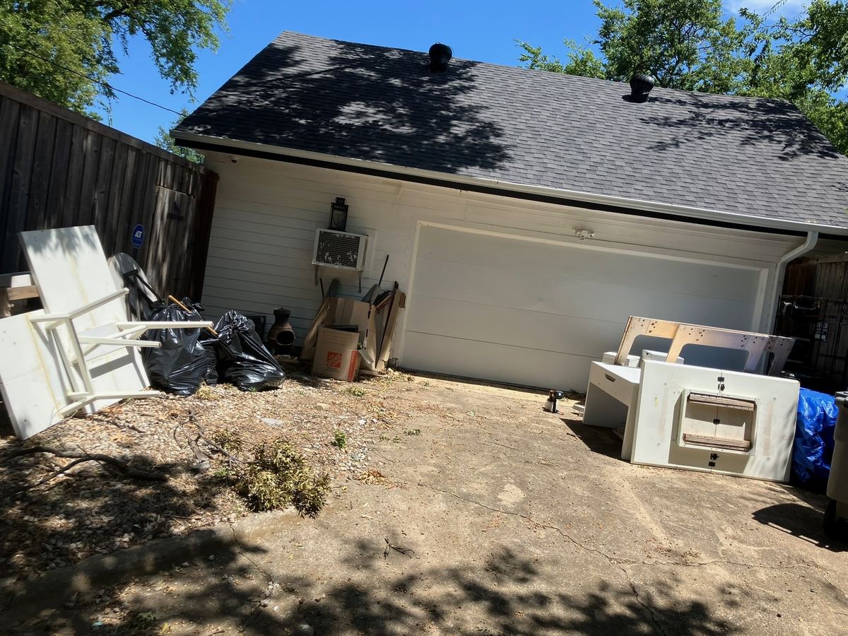 Old tables, trash bags and boxes piled beside a detached garage