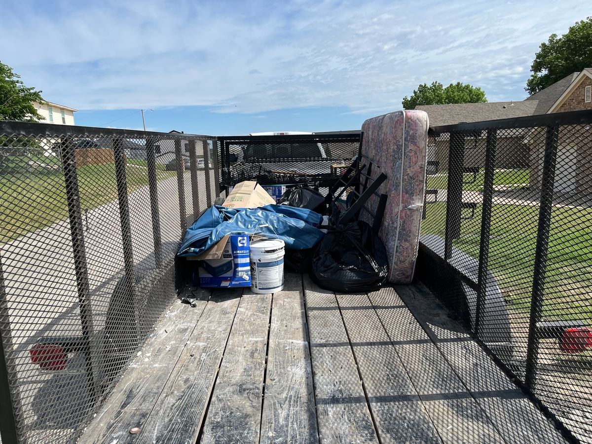 Mattress, bed frame, an air mattress, trash bags and a paint bucket loaded on a hauling trailer