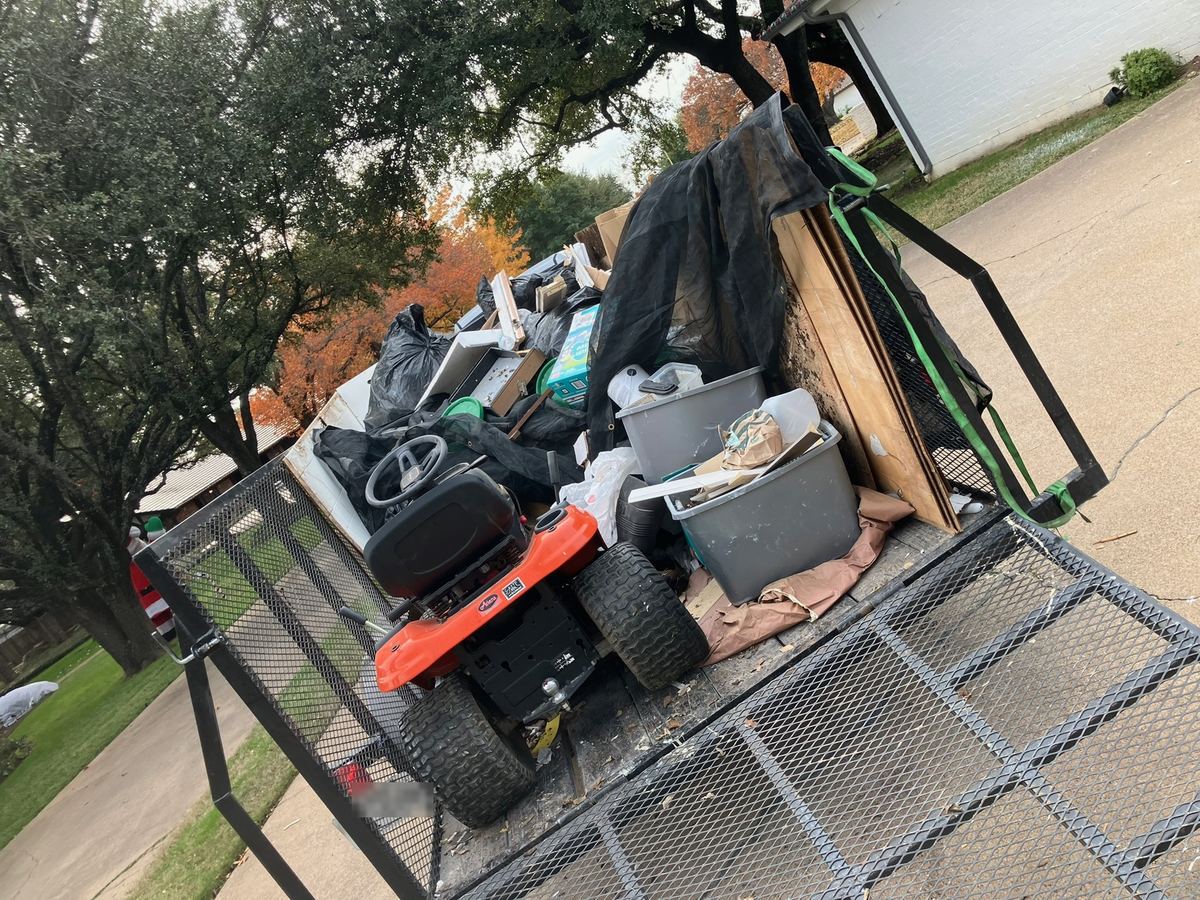Trailer loaded with a riding lawn mower, plastic bins, plywood and trash bags
